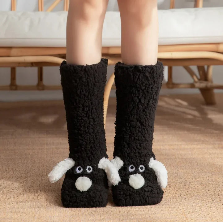 Black fuzzy slippers with cartoon face design worn indoors. Close-up of plush dog sock design showing soft material and cute dog pattern